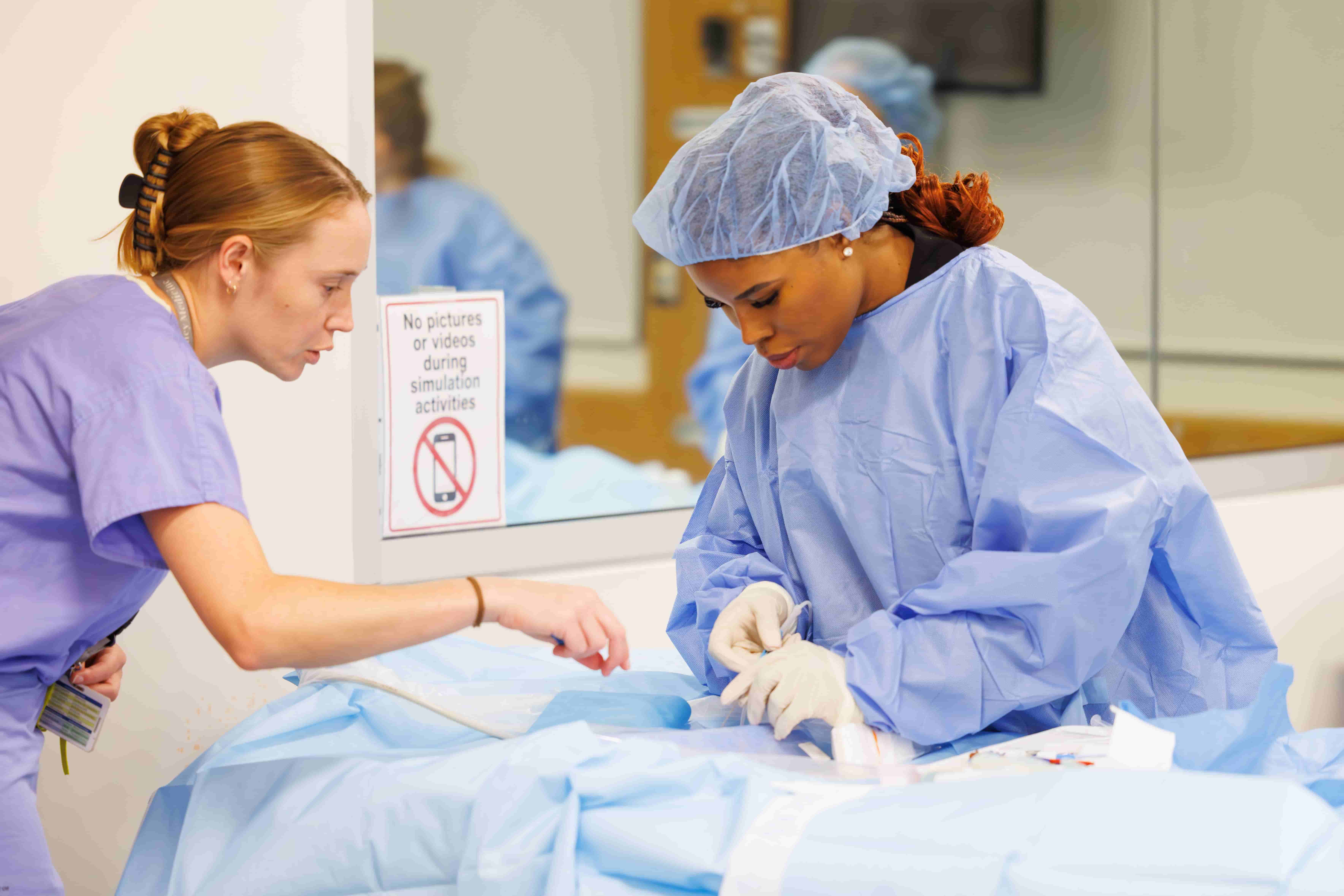 Emergency Medicine intern Dr. Linda Onyirimba practices a procedure on a simulation patient as resident Dr. Lauren Hopper provides guidance during orientation day in the simulation lab.